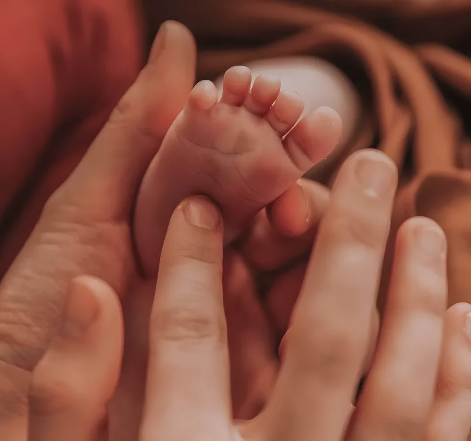 Pied de bébé tenu par un parent pendant l’atelier de réflexologie plantaire bébé