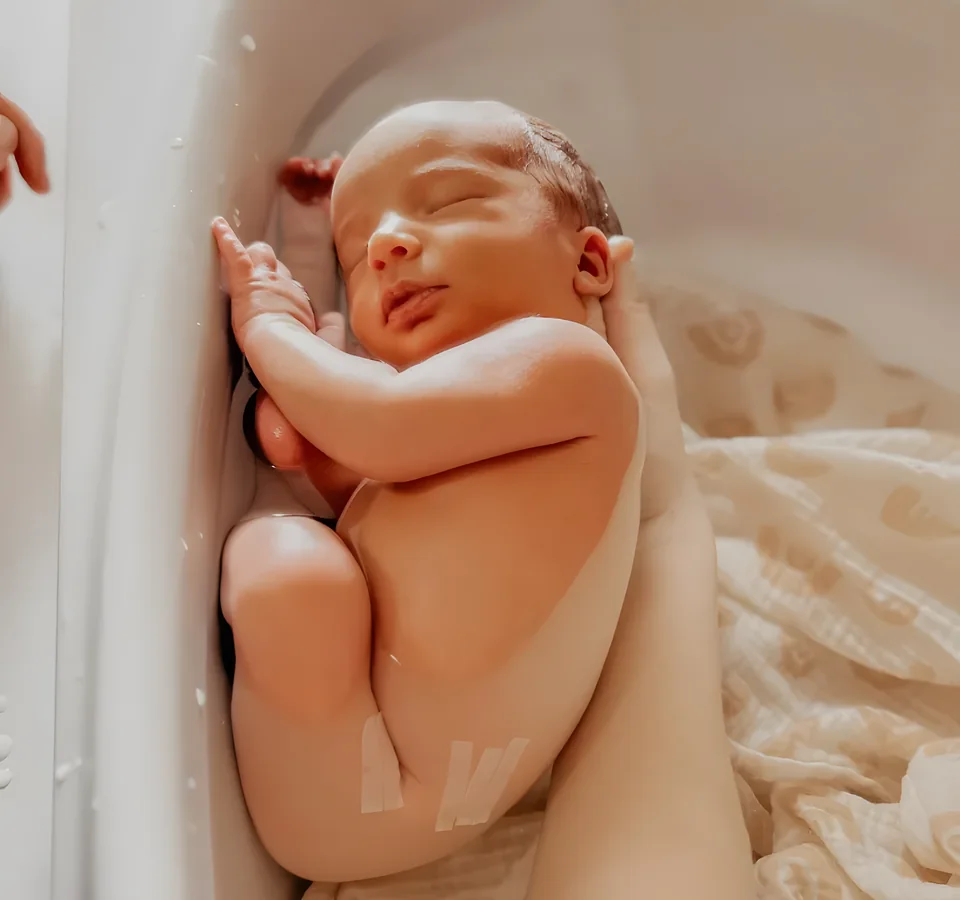 Nouveau-né endormi recroquevillé dans la baignoire pendant un bain bébé enveloppé